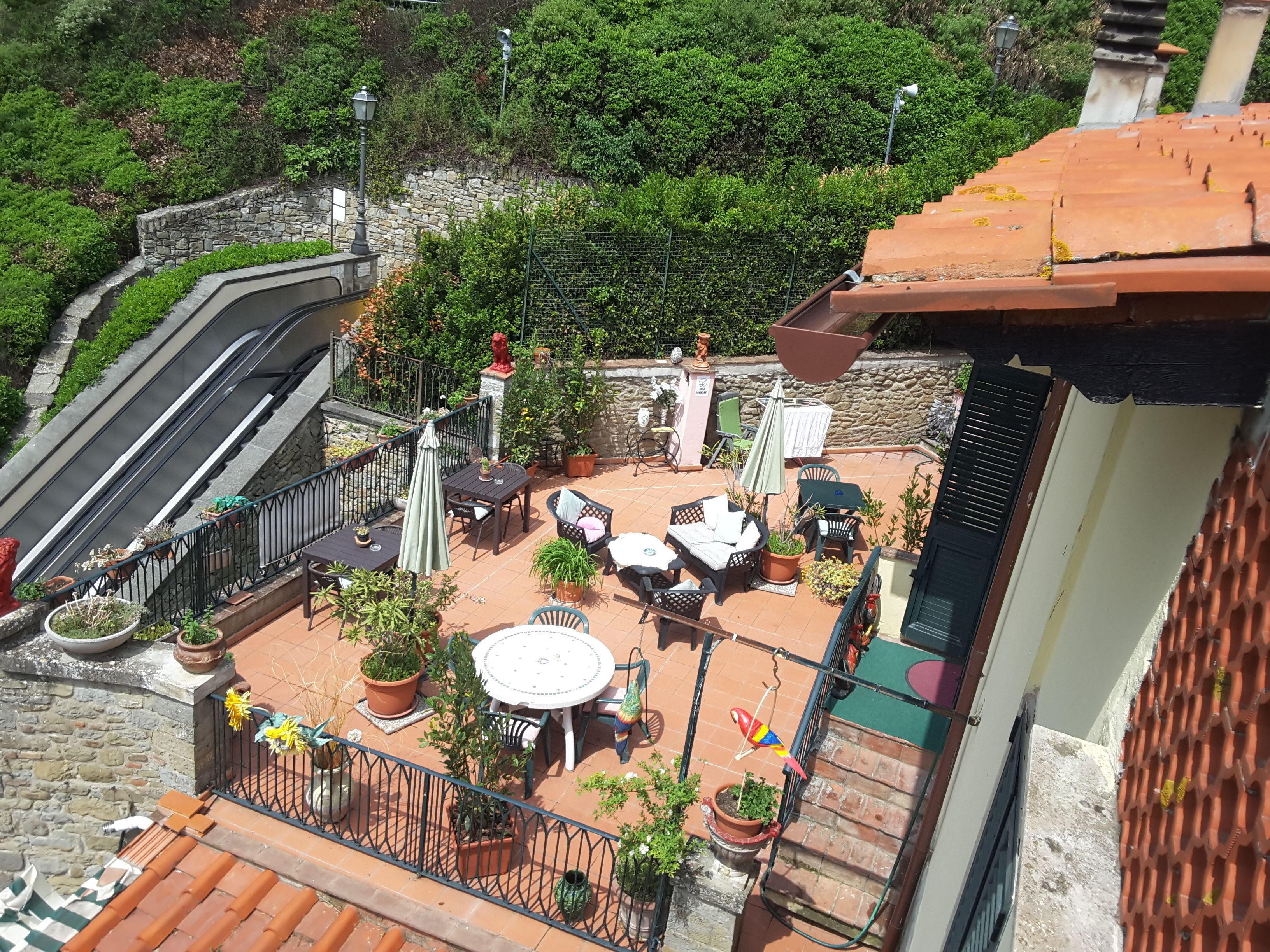 Una terraza en la azotea con mobiliario exterior, plantas en macetas y un muro de piedra.