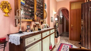 A hallway with a wooden cabinet displaying figurines, a brass trumpet, and framed pictures. - Casa Kita (Cortona)