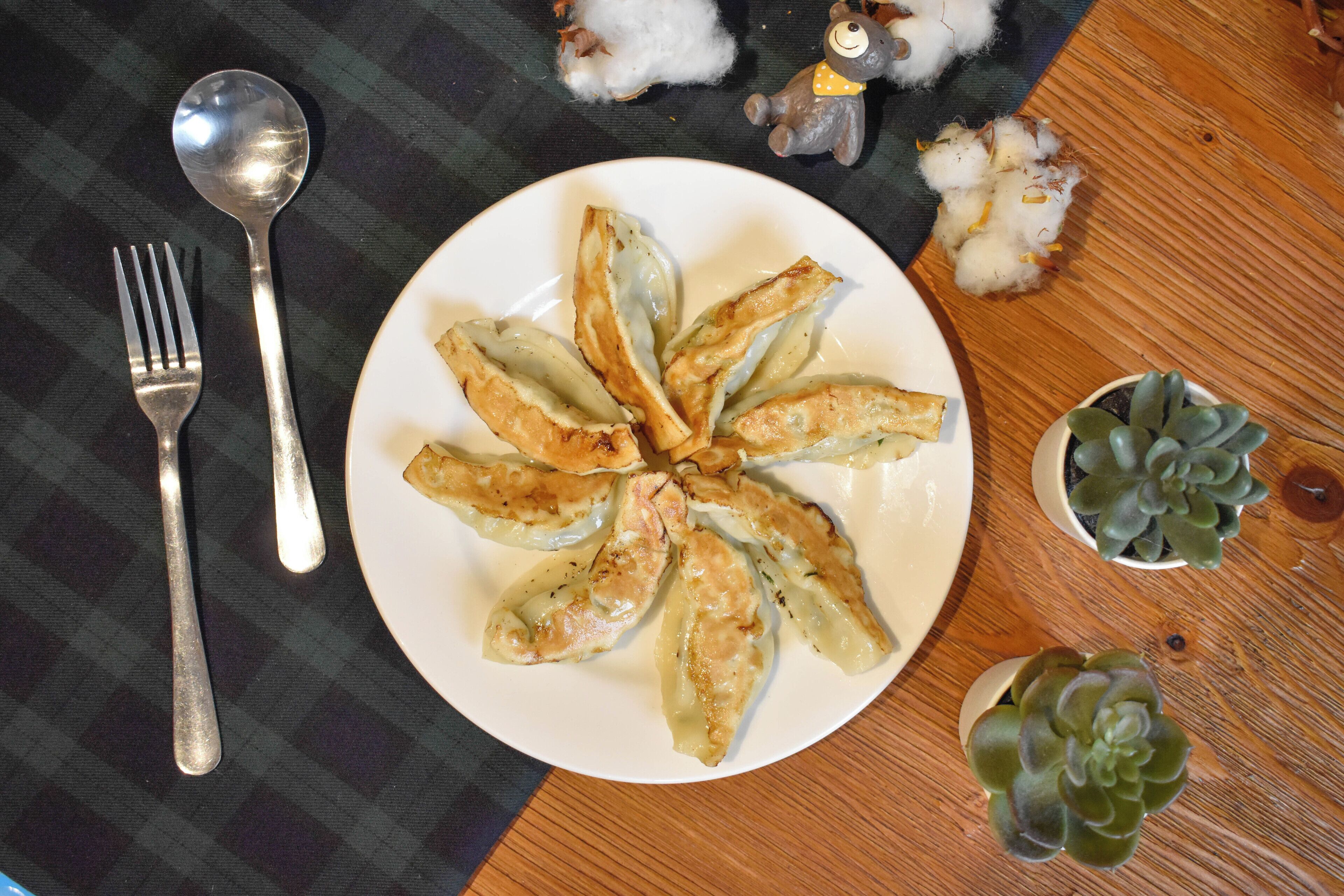 A plate of dumplings on a table with a fork, spoon, and two small potted plants.