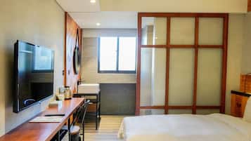 Une chambre d’hôtel avec un lit, un bureau avec une télévision, une fenêtre et une porte coulissante.