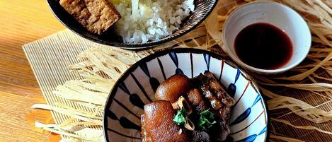 Une table en bois sur laquelle reposent deux bols de nourriture : l’un contient du riz et de la viande, et l’autre, un autre plat de viande. Les deux bols sont posés sur un tapis tissé.