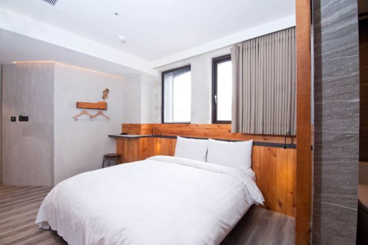 Een moderne slaapkamer met een houten hoofdbord, een groot bed en een raam met gordijnen.