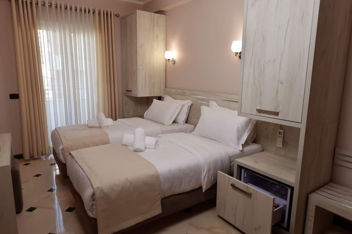 Una habitación de hotel con dos camas, un armario de madera, una mesita de noche y una caja fuerte empotrada.