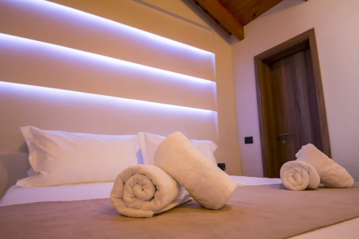Una cama bien hecha con toallas enrolladas y un cabecero de madera con iluminación integrada.