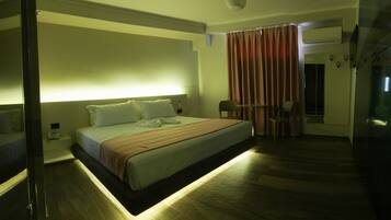 Habitación de hotel con una cama grande, una mesita de noche, una silla, un escritorio y un equipo de aire acondicionado.