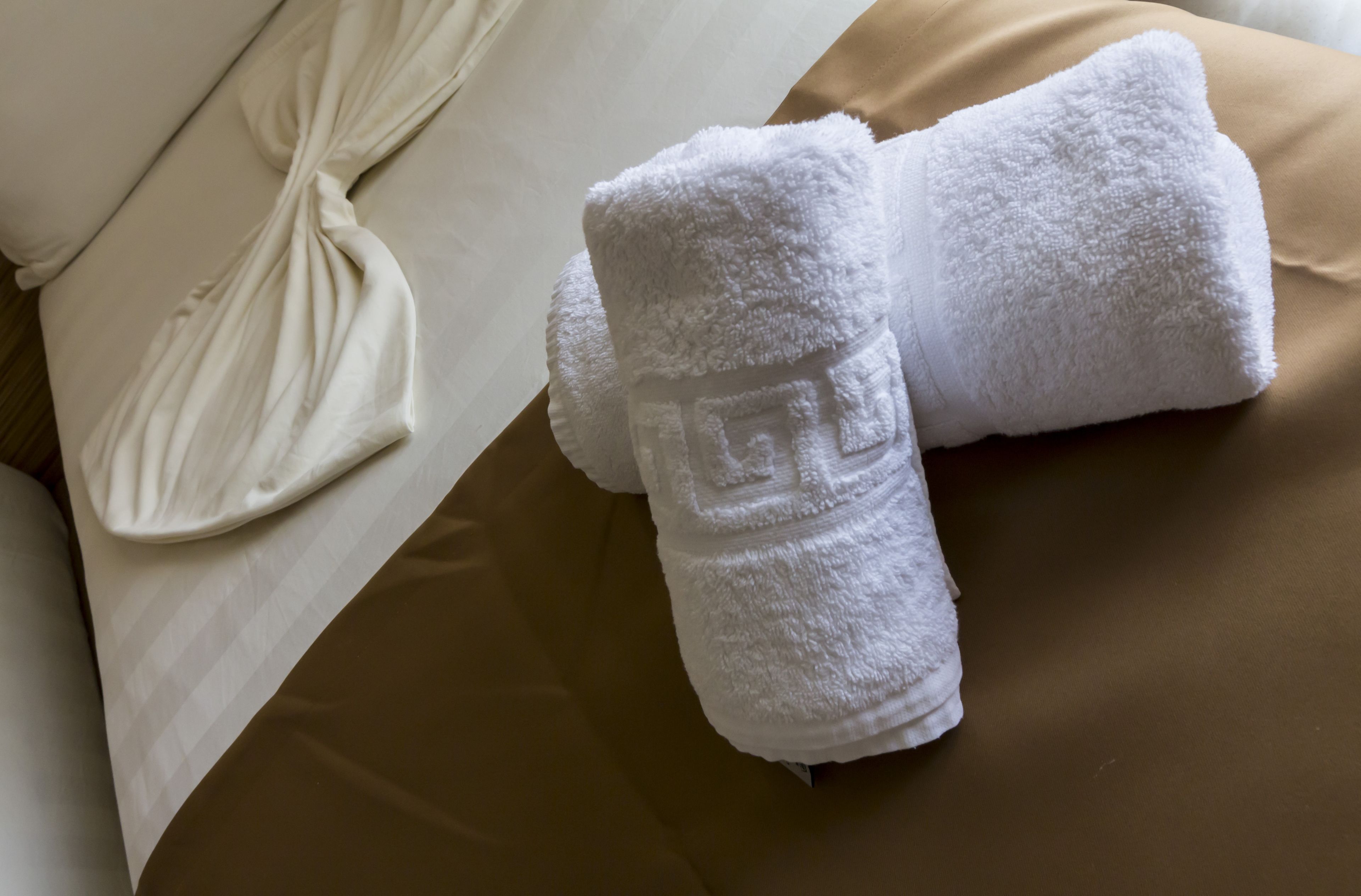 A neatly made bed with a white pillow and two folded white towels.