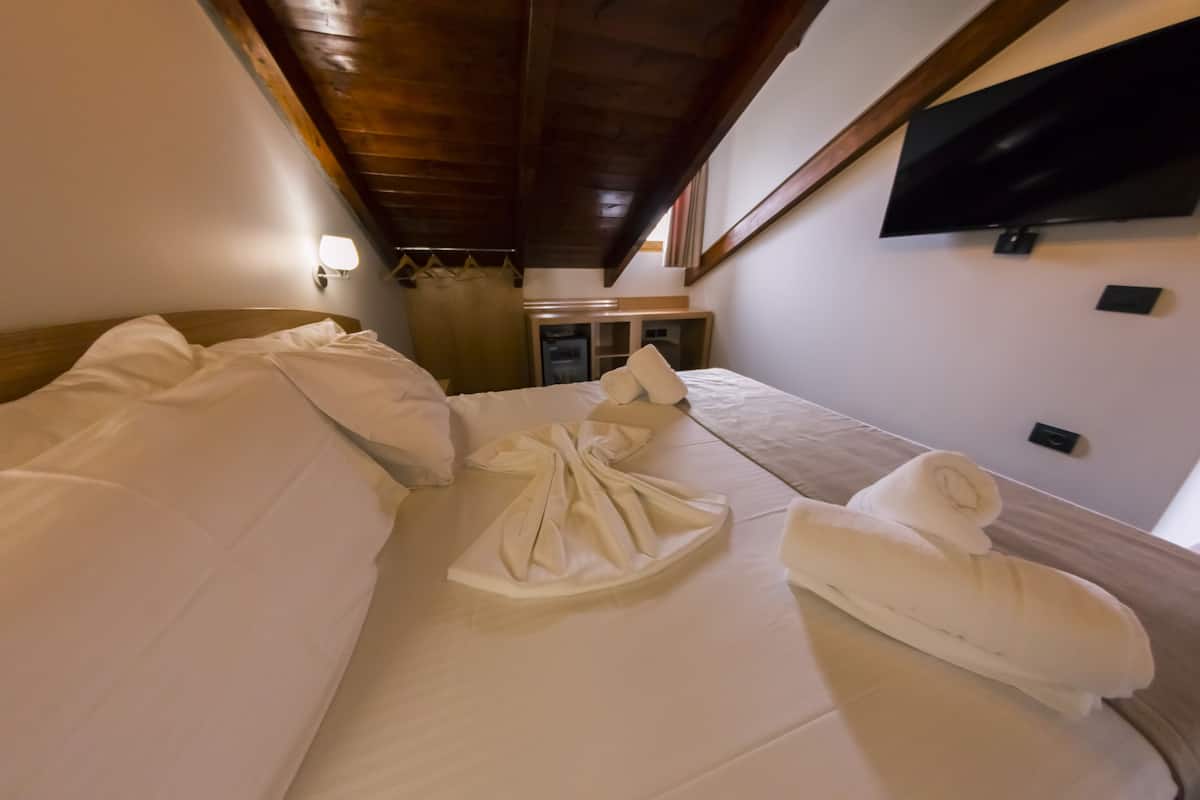 Una habitación de hotel con una cama, un televisor en la pared y una mesita de noche con una lámpara.
