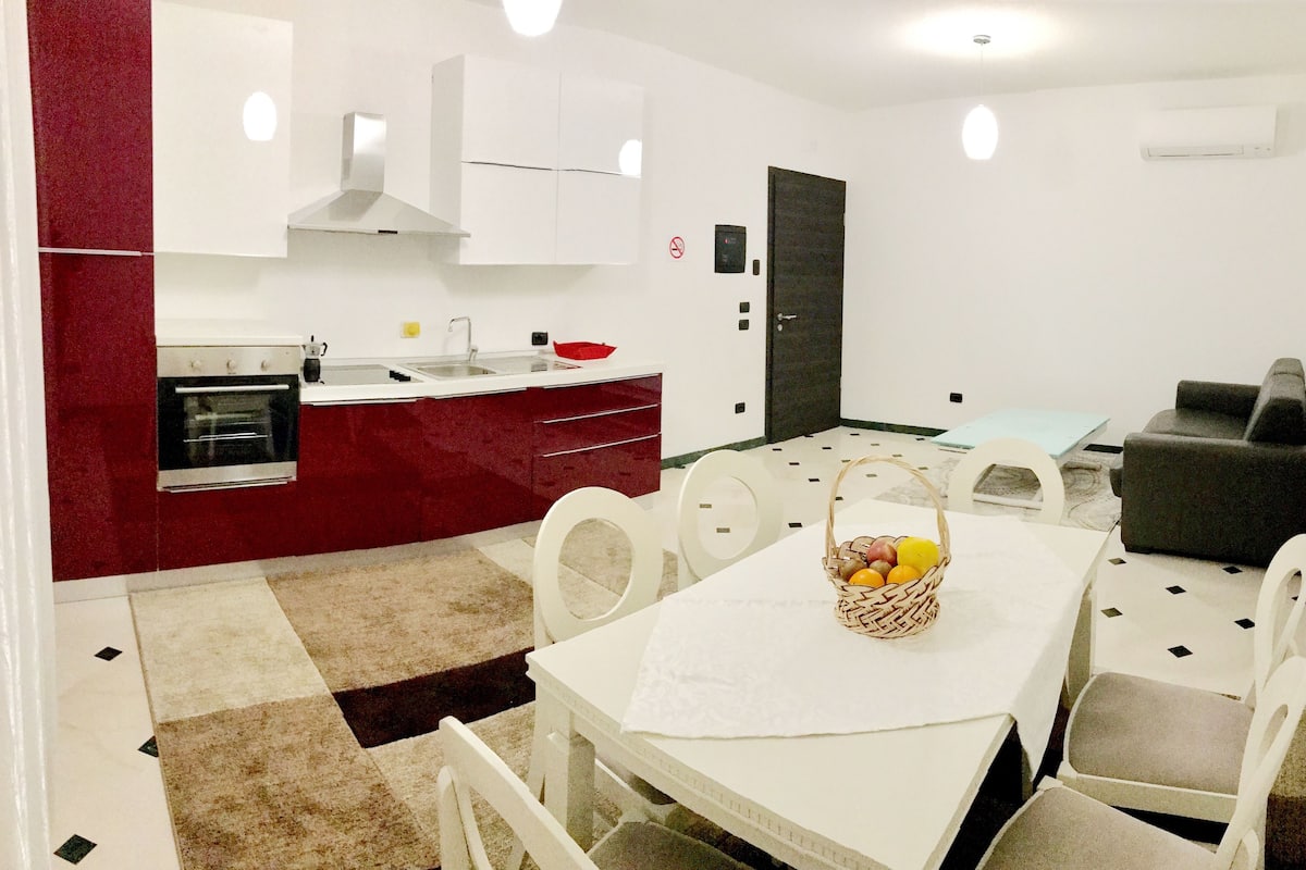 Una cocina moderna con armarios blancos, una pared de acento roja y un comedor con sillas blancas y una mesa.