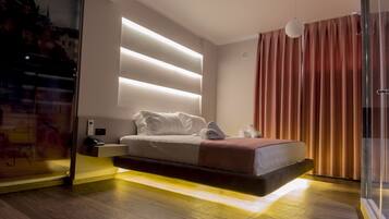 Habitación de hotel moderna con cama, mesita de noche y vistas a un paisaje urbano a través de un muro de cristal.