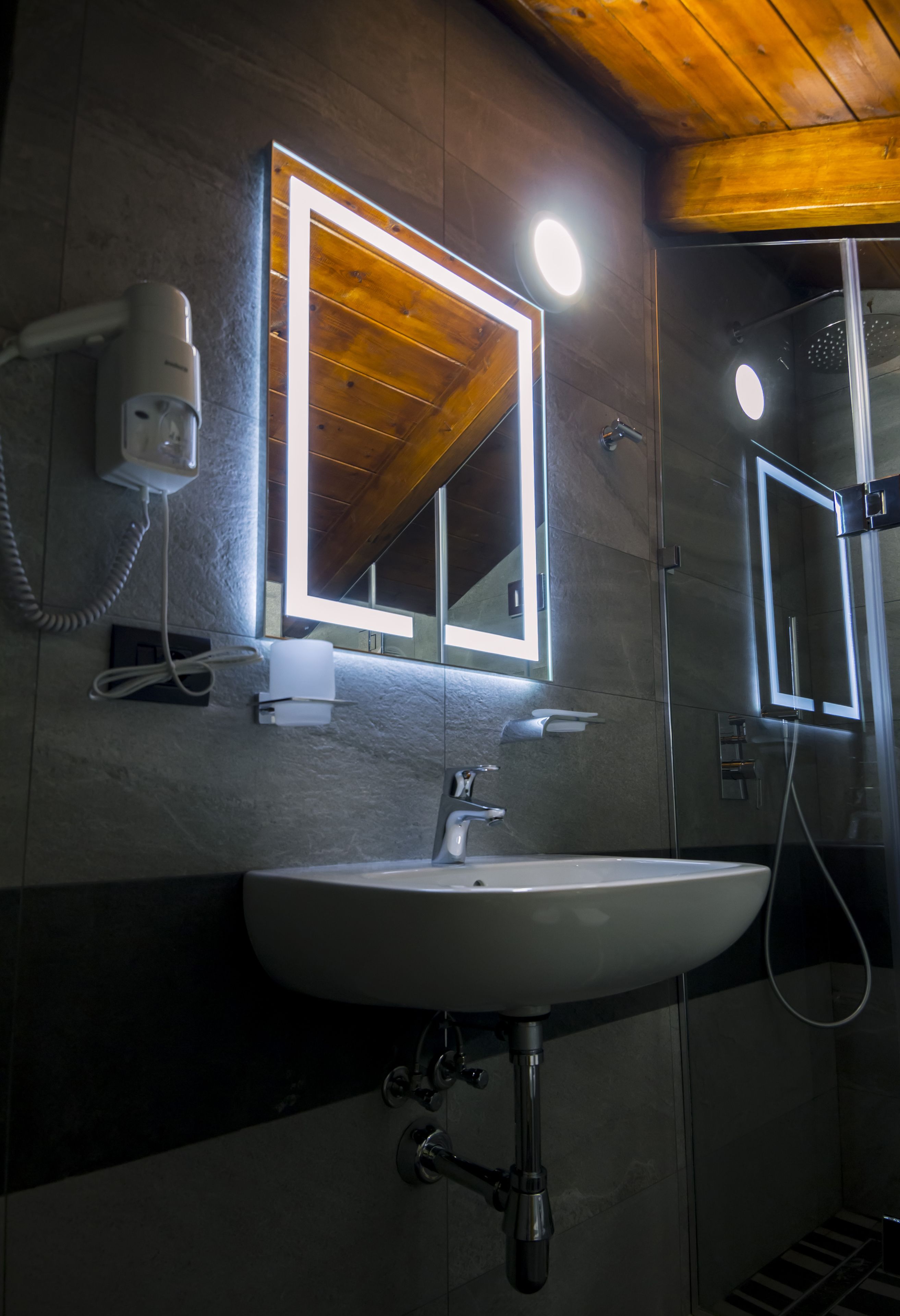 Un baño con lavamanos blanco, un espejo con luces, secador de pelo y ducha.