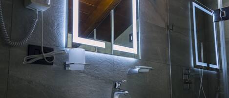 Un baño con lavamanos blanco, un espejo con luces, secador de pelo y ducha.