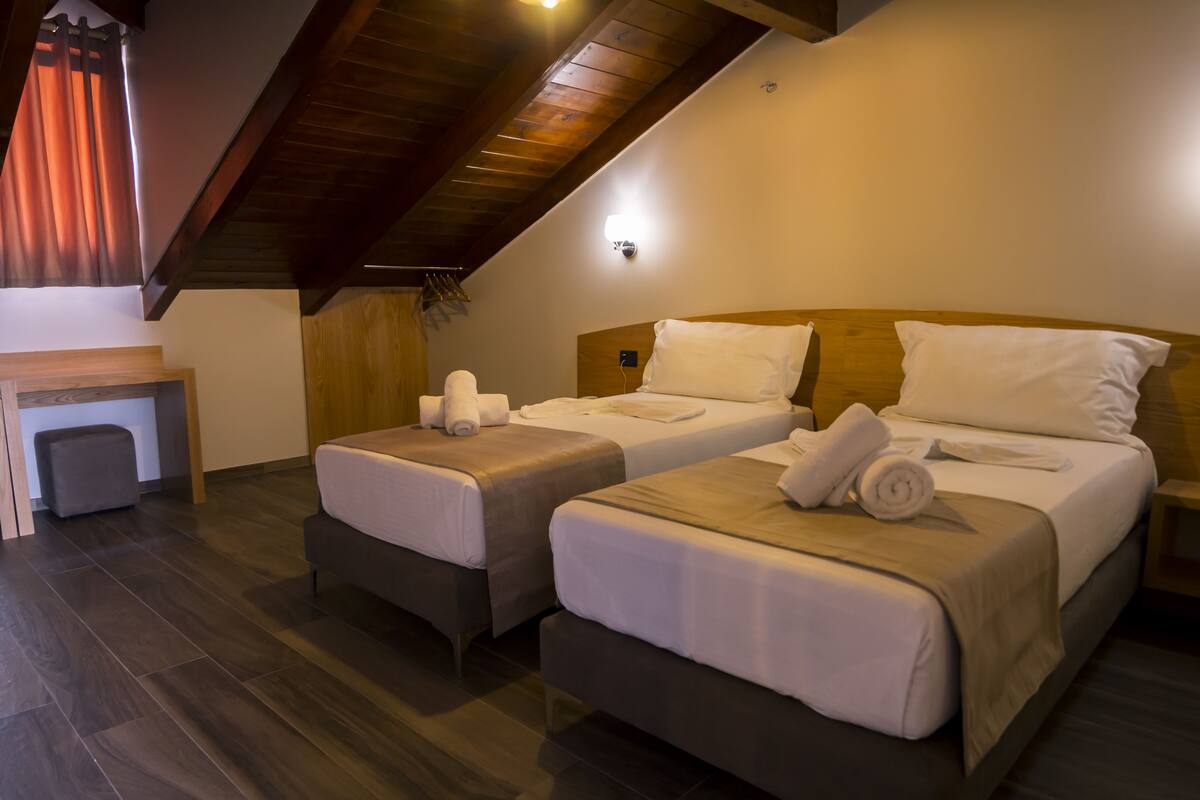 Una habitación con dos camas individuales, cabeceros de madera, una mesita y un banco.