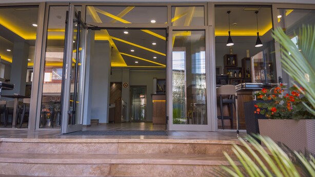 A modern building entrance with glass doors, a staircase, and a seating area visible through the glass. - Hotel Pandora Residence (Tirana)