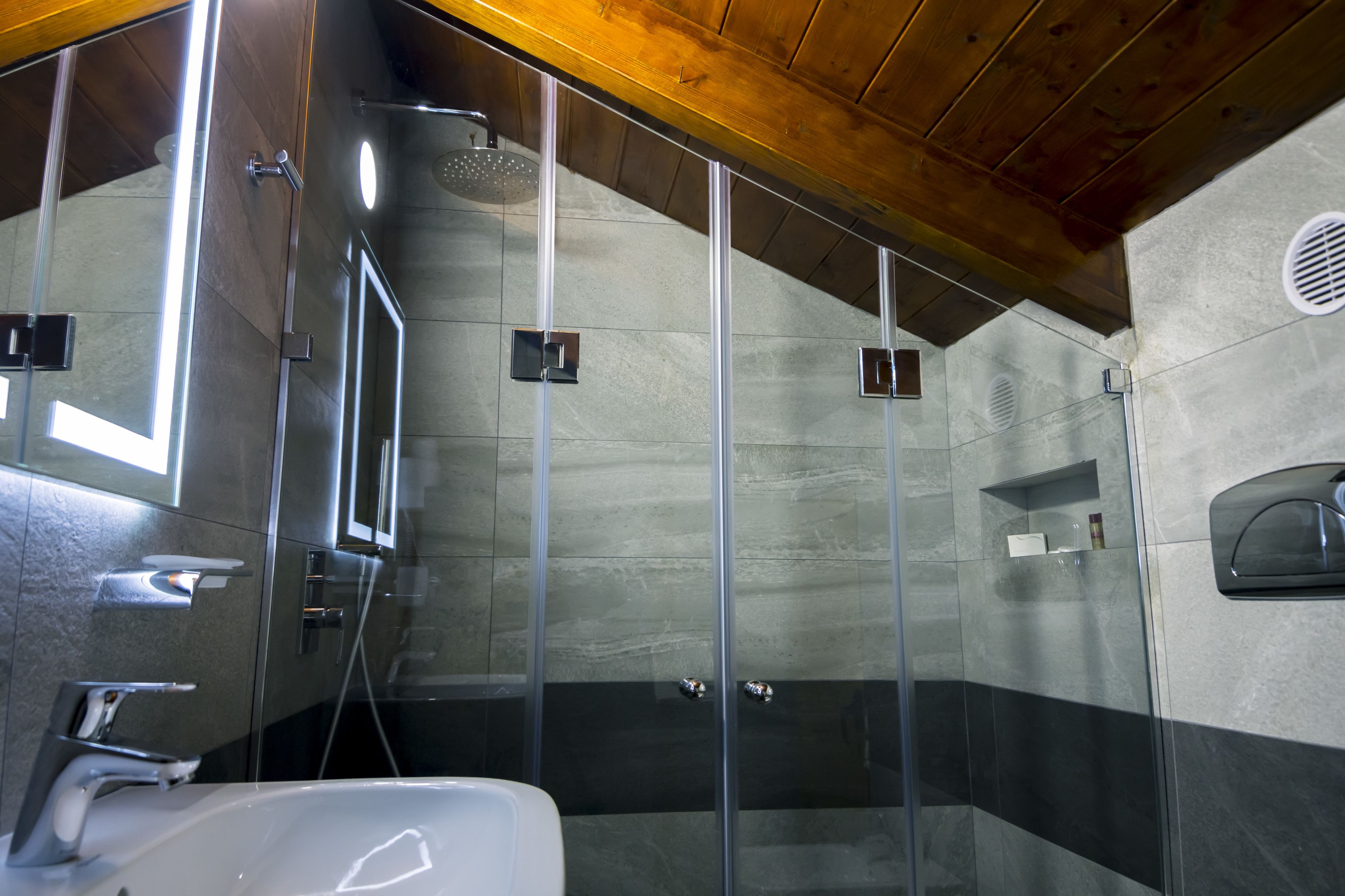 A modern bathroom with a glass shower enclosure, a sink, and a wooden ceiling.