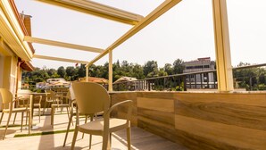 A terrace with chairs and tables, a wooden railing, and a view of buildings and trees. - Hotel Pandora Residence (Tirana)