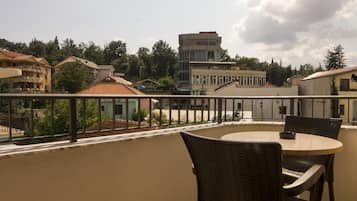 A balcony with wicker chairs and a table, overlooking a residential area with houses and a tall building.