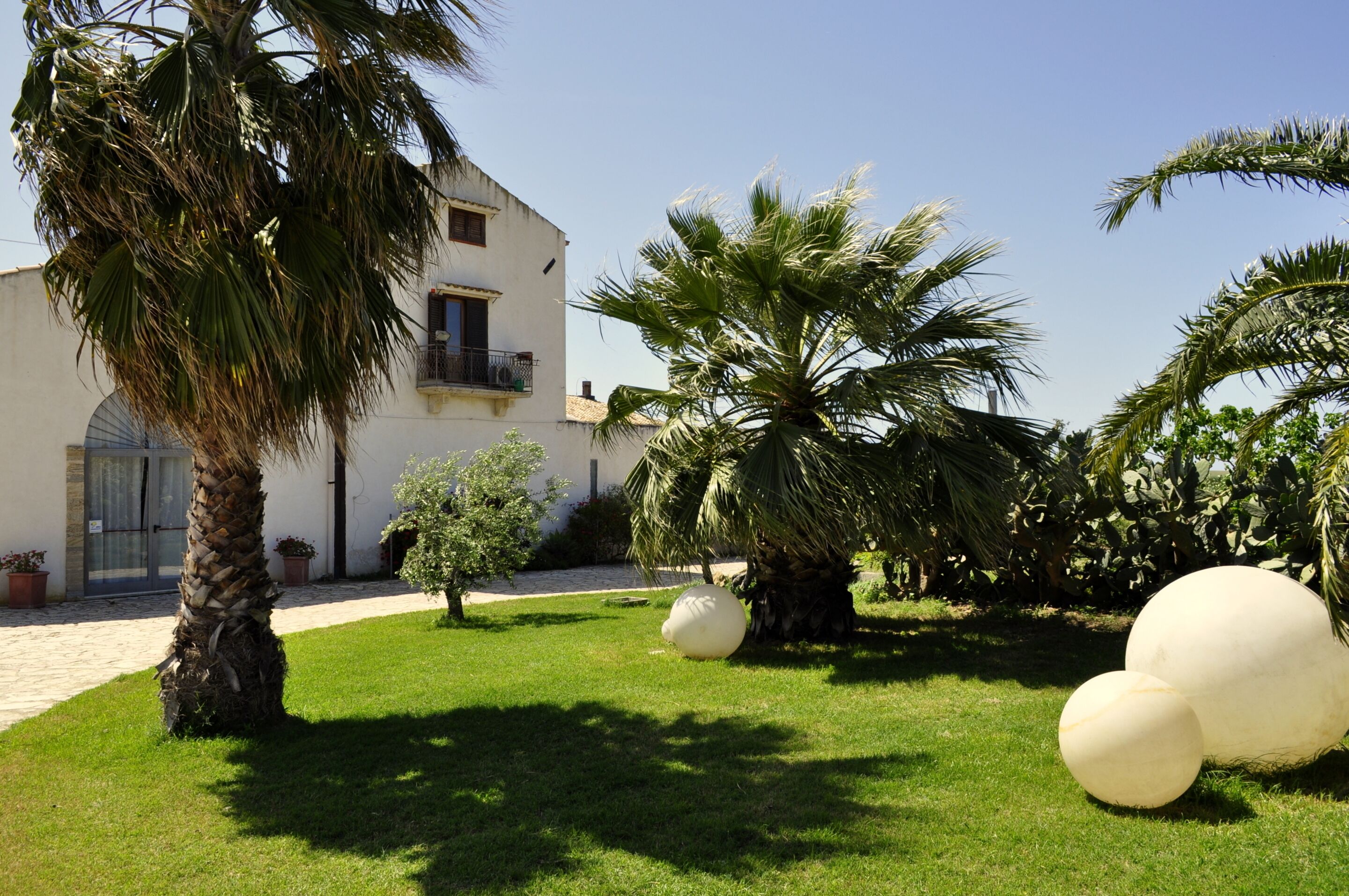 A building with a white facade, a palm tree, and a small garden with spherical sculptures.
