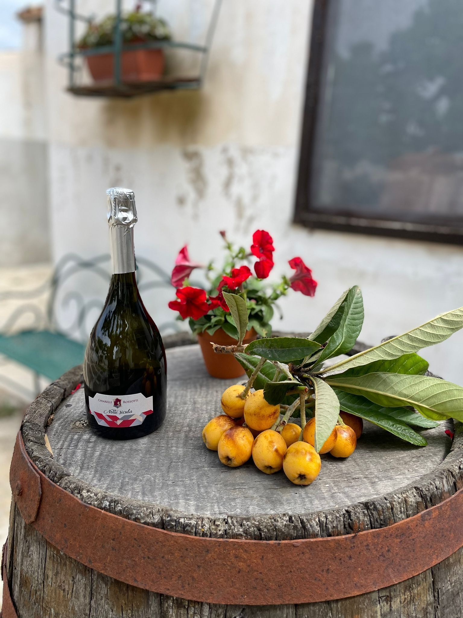A bottle of wine, red flowers, and yellow fruits on a wooden surface.