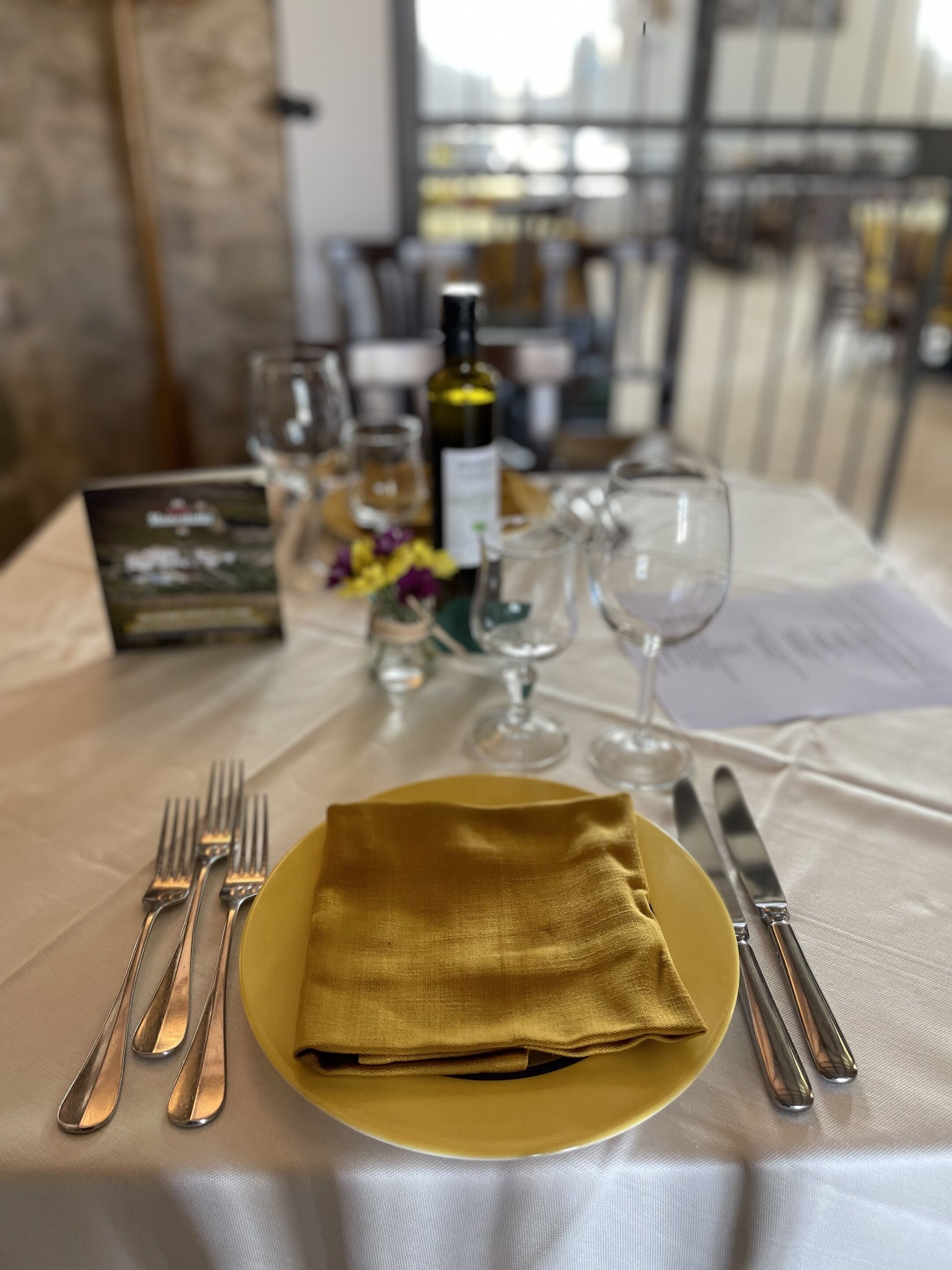Un tavolo apparecchiato con un tovagliolo piegato, posate e una bottiglia di vino.