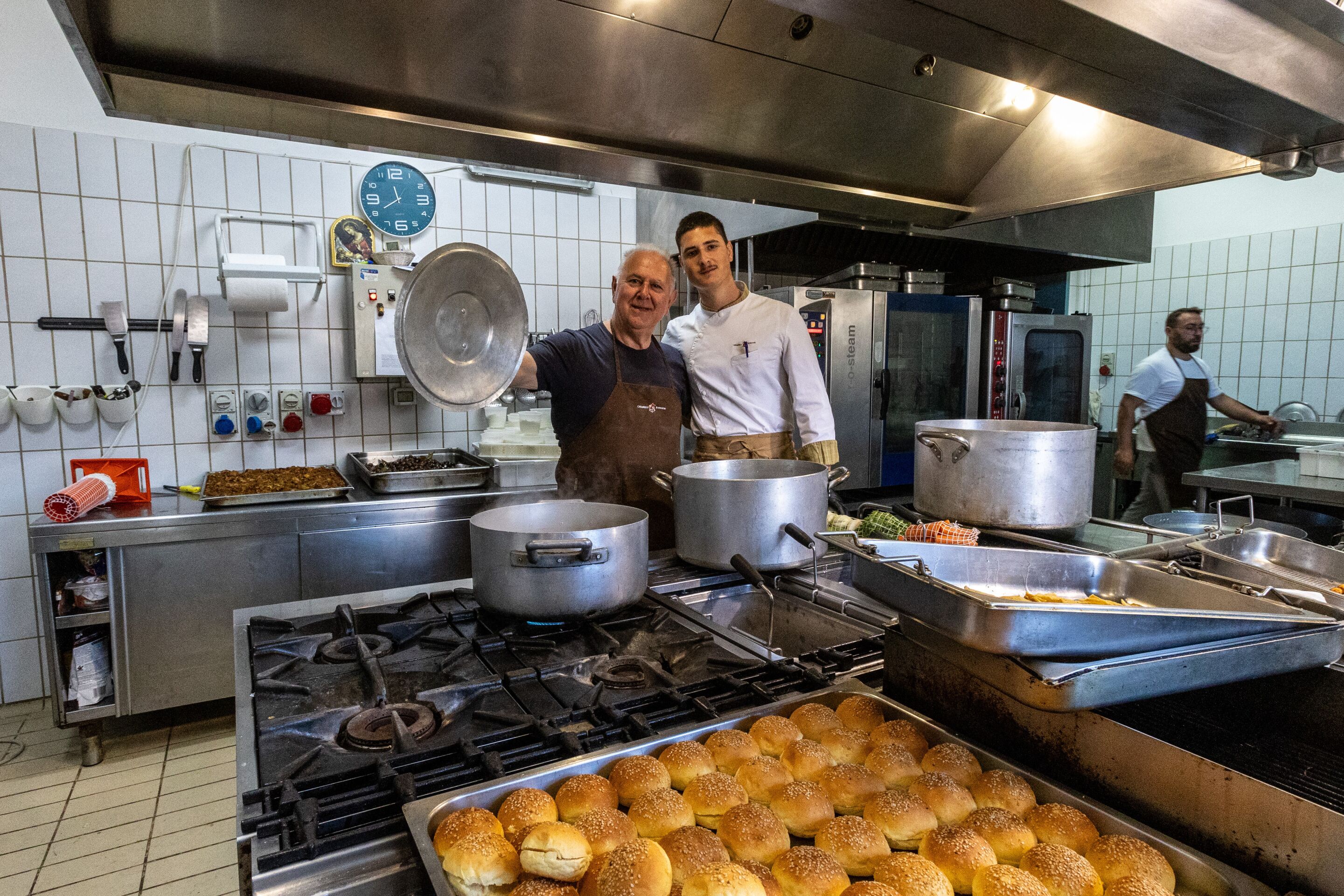 Una cucina professionale con elettrodomestici in acciaio inossidabile, un orologio e un vassoio grande pieno di pane.