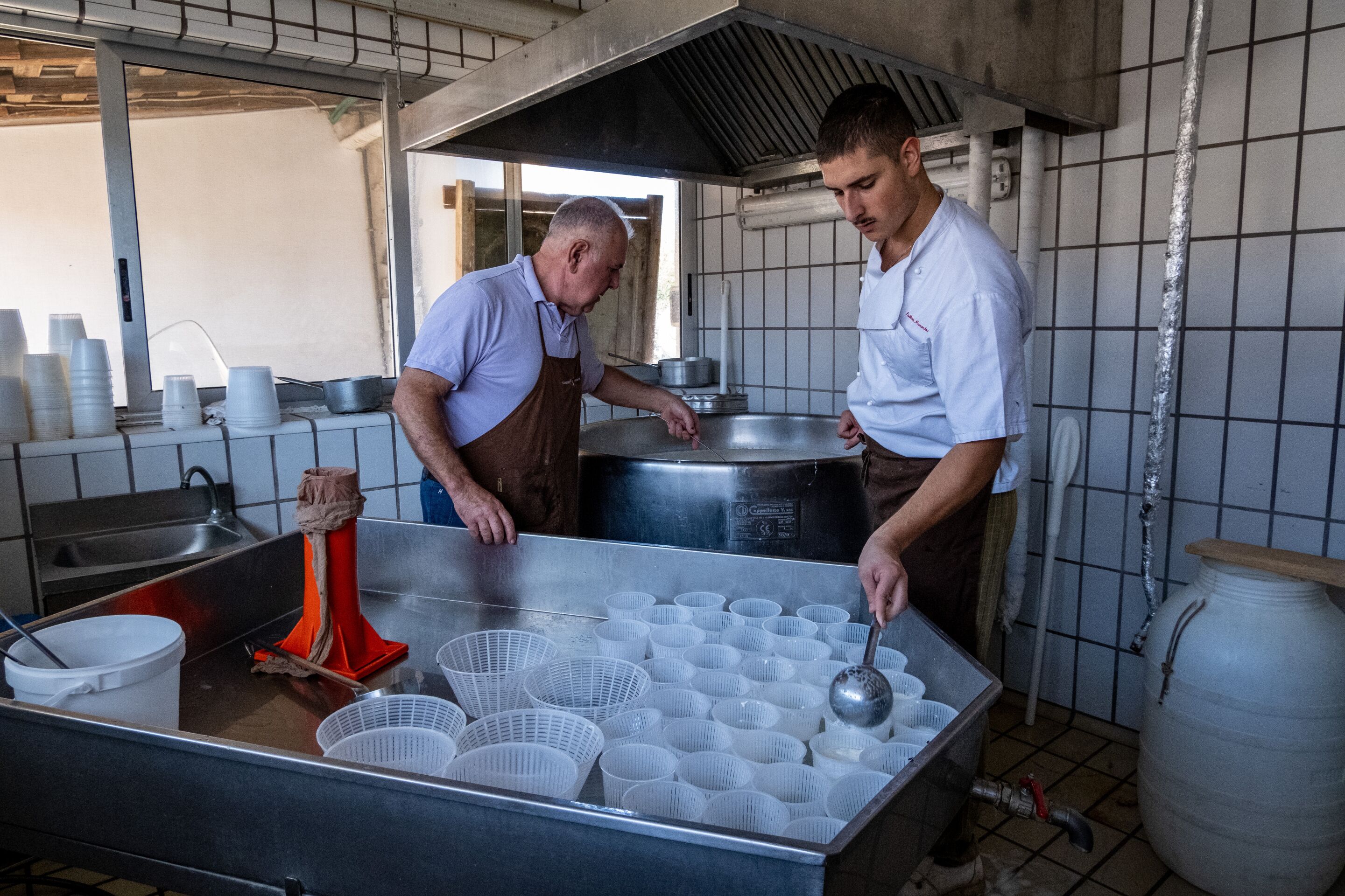 A commercial kitchen with stainless steel surfaces, a large pot, and multiple plastic containers.