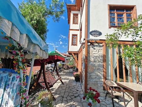 A narrow street with a café, outdoor seating, and a stone building with a wooden door.