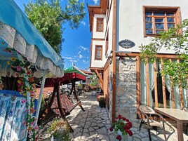 Una calle estrecha con un café, mesas al aire libre y un edificio de piedra con puerta de madera.