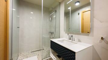 A modern bathroom with a glass-enclosed shower, a white sink with a black textured cabinet, and a mirror above the sink.