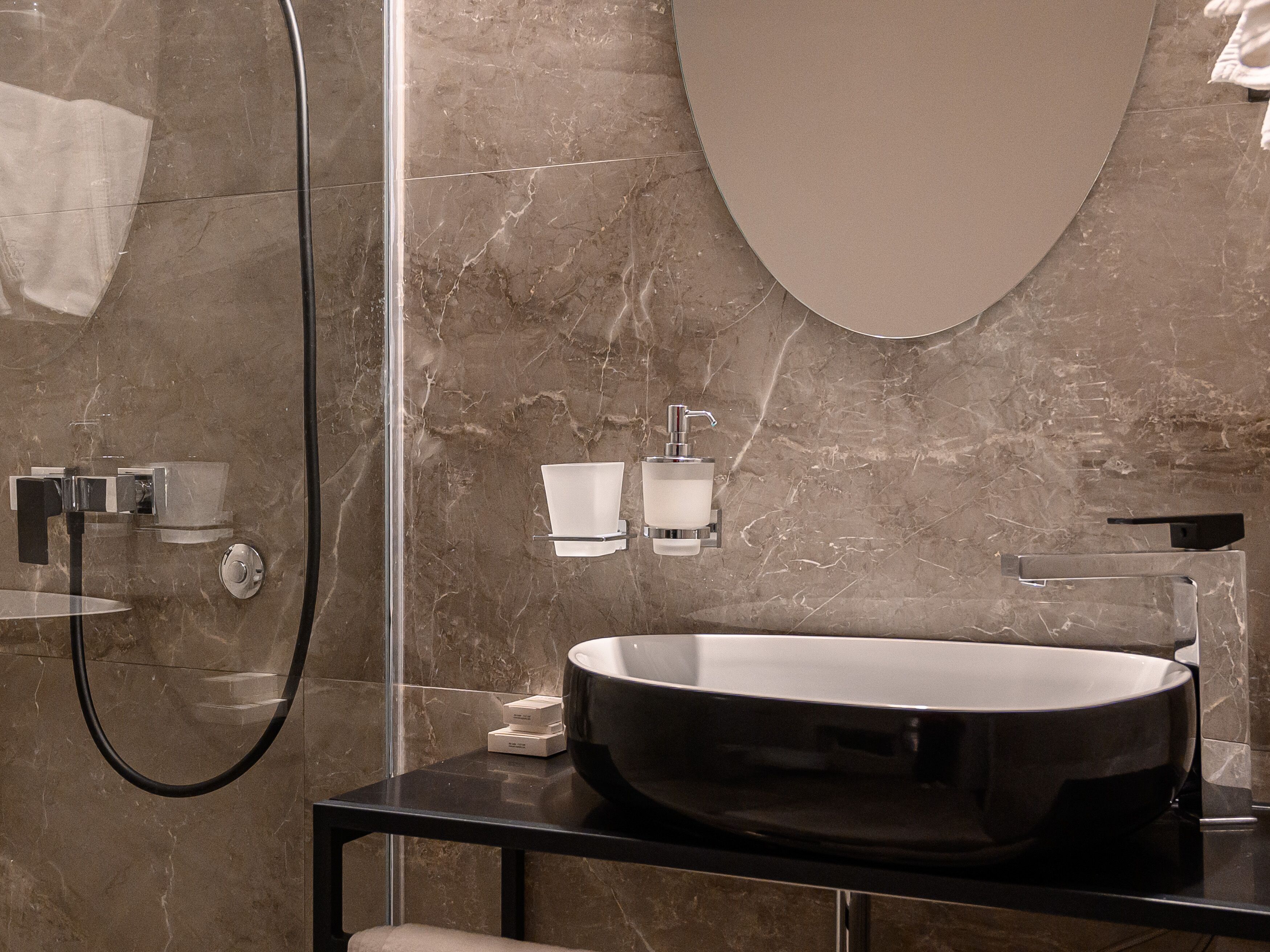 Un baño moderno con un lavabo ovalado grande, cabina de ducha con paredes de vidrio y un revestimiento de mármol.