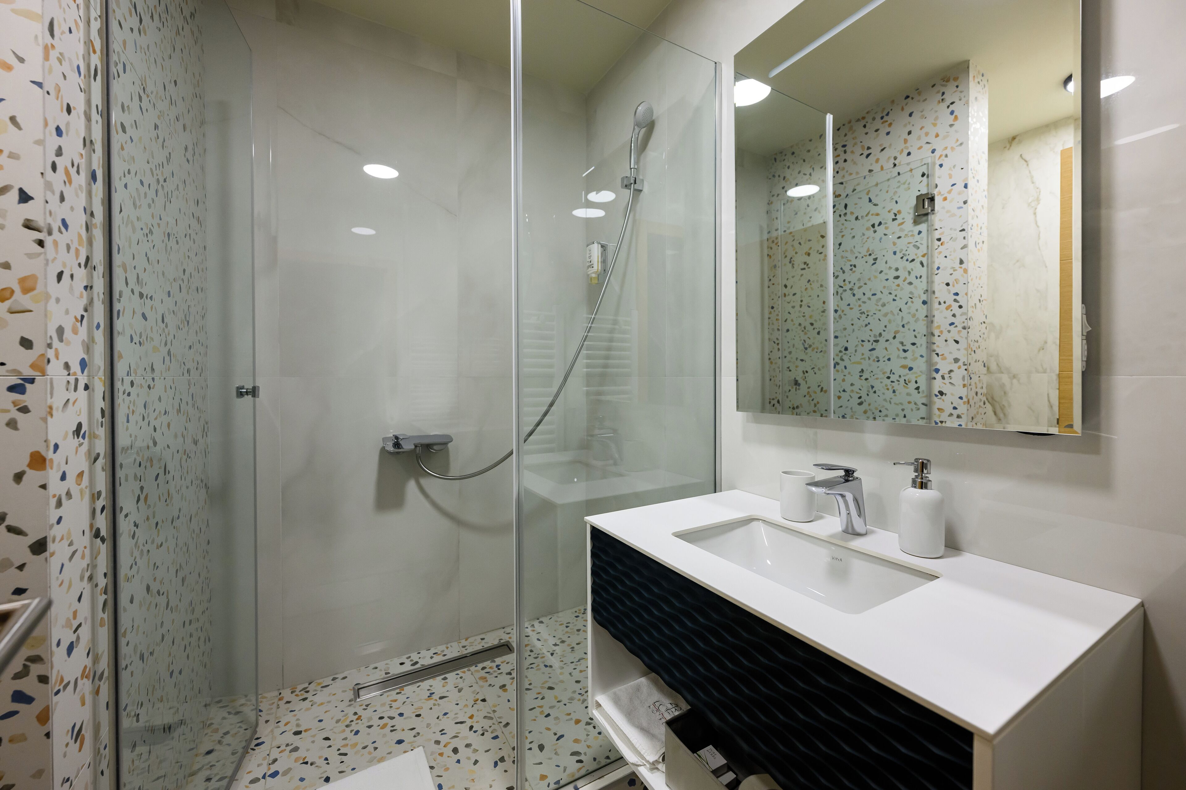 Un bagno moderno con doccia vetrata, un lavandino bianco e uno specchio grande.