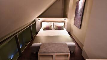 A narrow, dimly lit room with a bed, bedside tables, and a wall-mounted artwork.