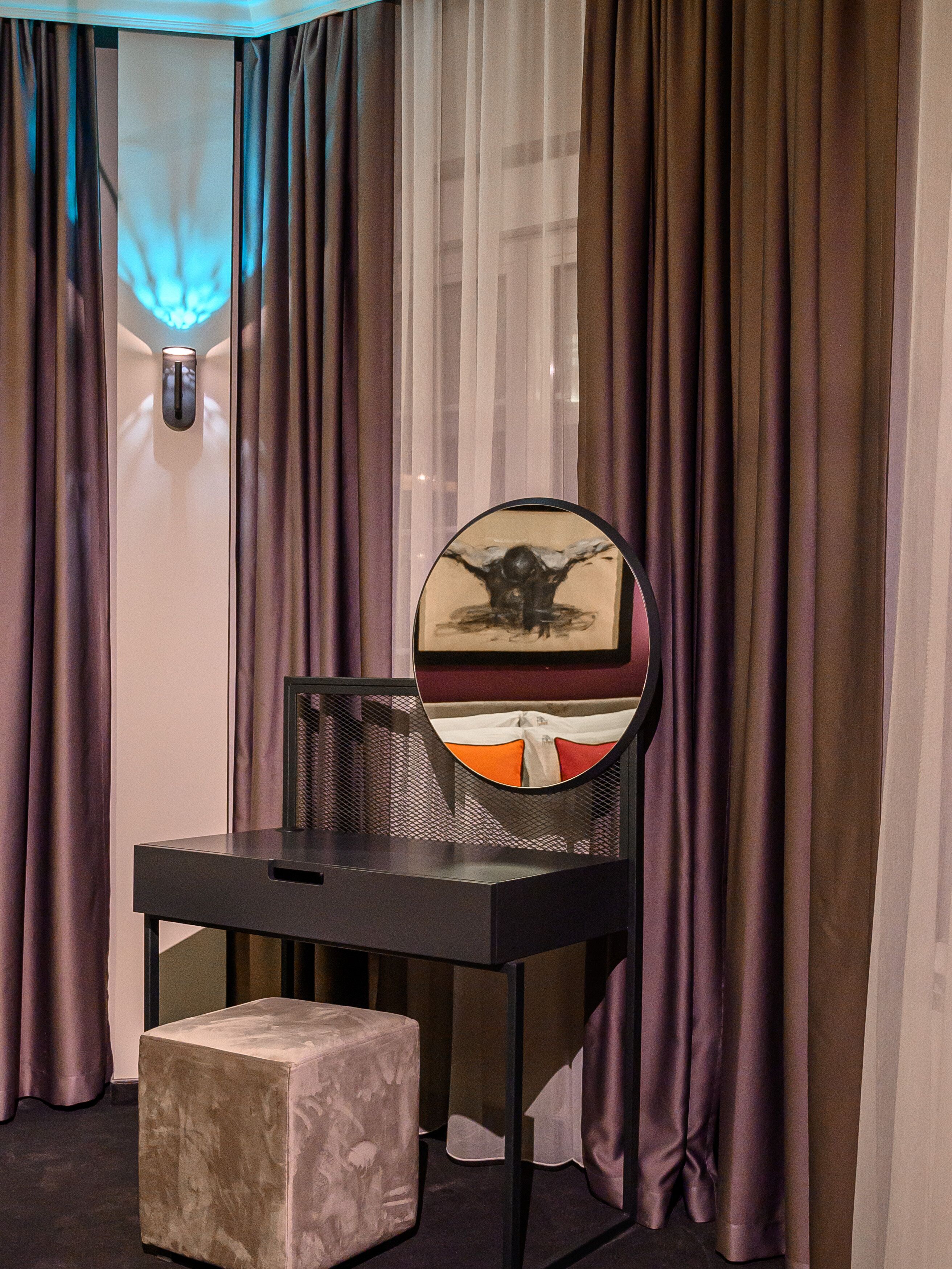 A room with a black desk, a round mirror, and a cushioned stool.