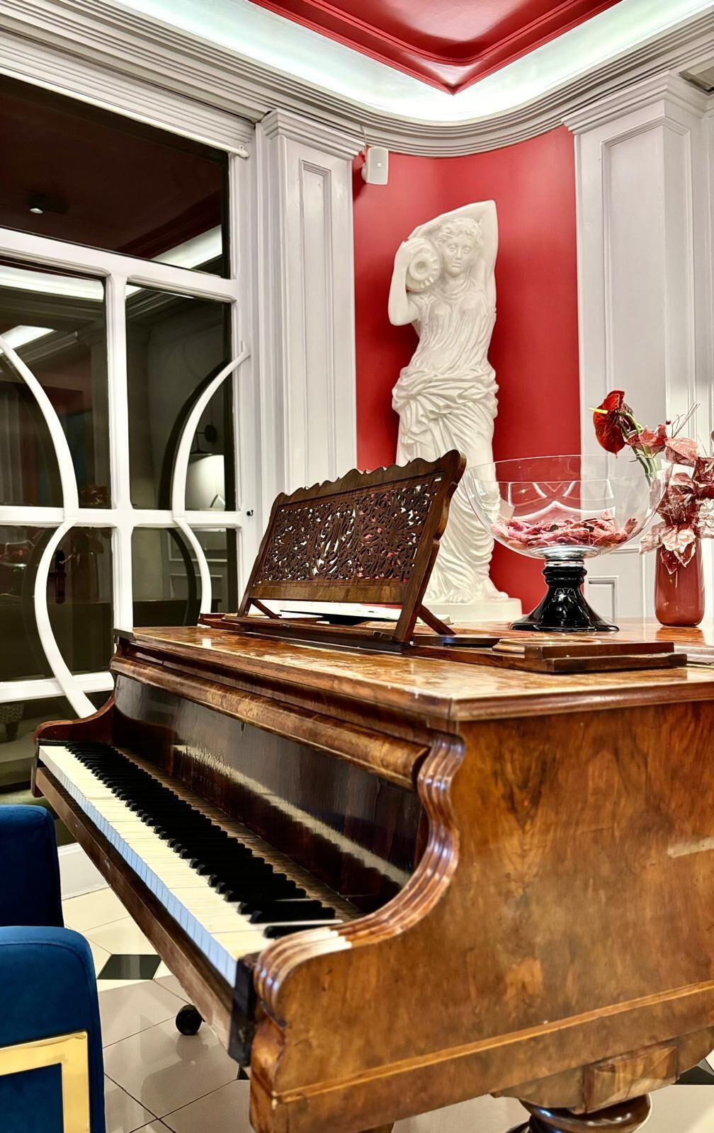 Un piano de cola en una habitación con una pared roja decorativa y una estatua blanca.