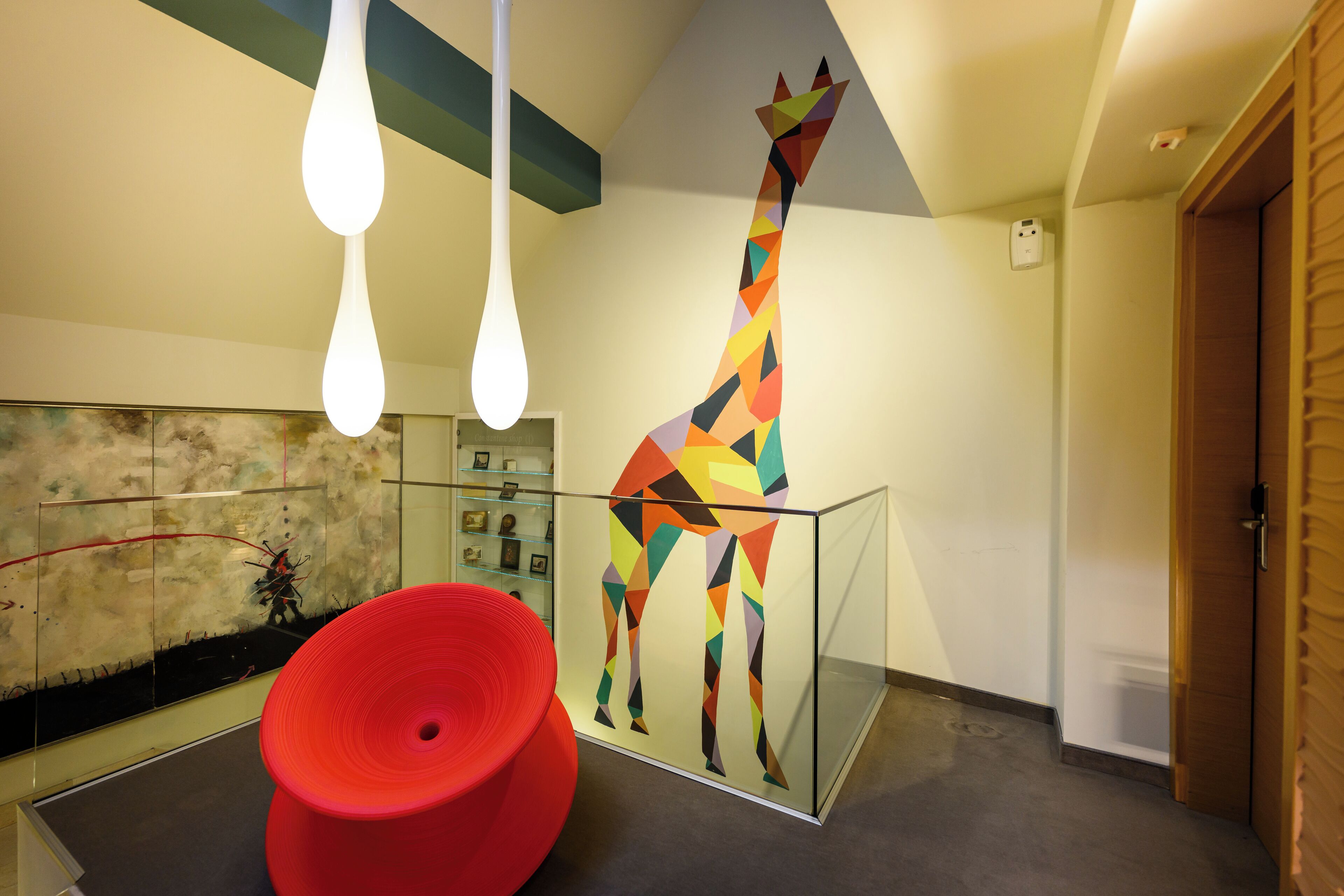 Un interior moderno con un mural de una jirafa colorida, una silla circular roja y un panel de vidrio.
