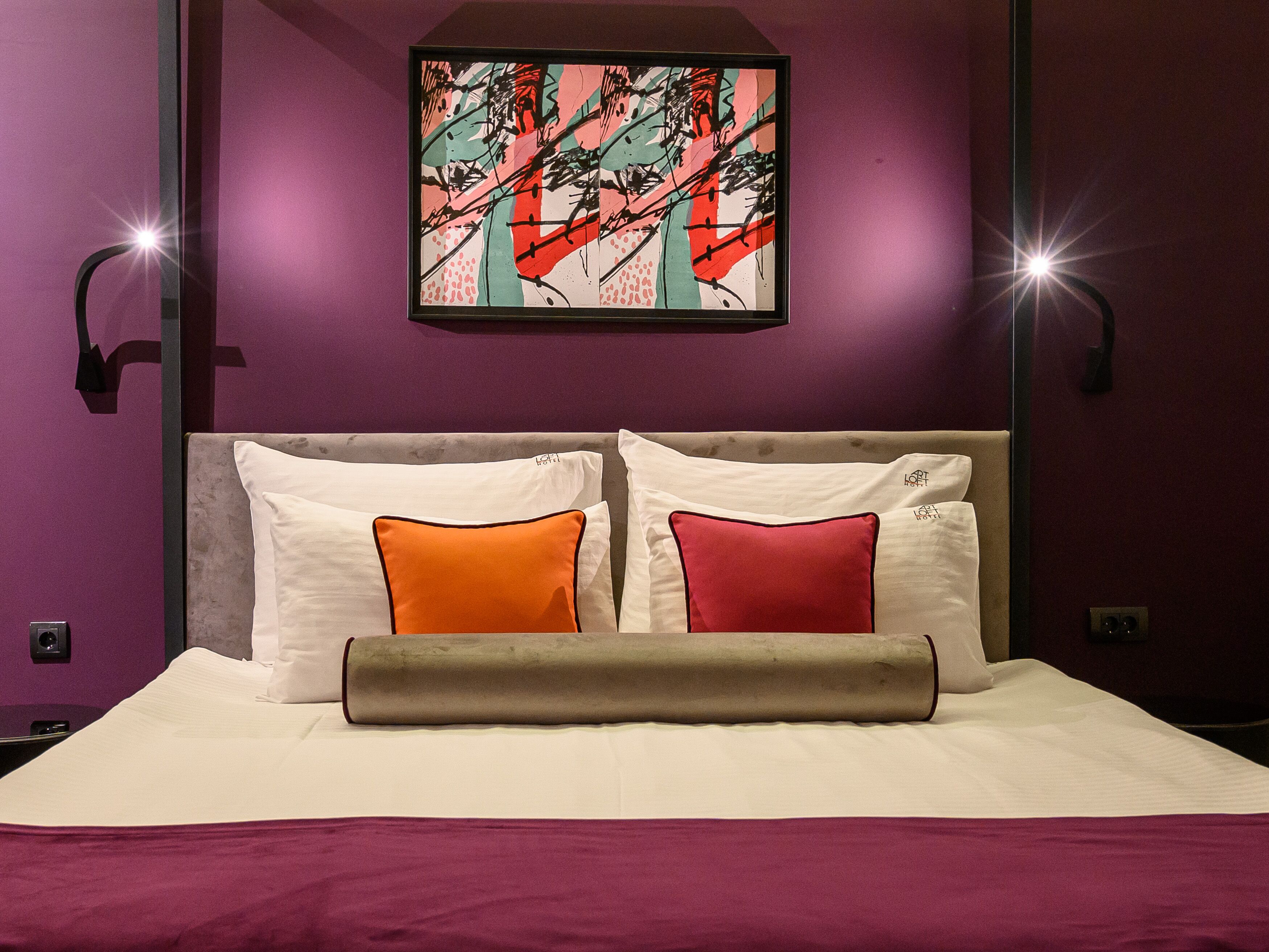 A hotel room with a bed, two pillows, a headboard, and a wall-mounted artwork.