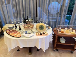 Una mesa servida para una comida con varios quesos, un queso entero grande y una botella de vino.