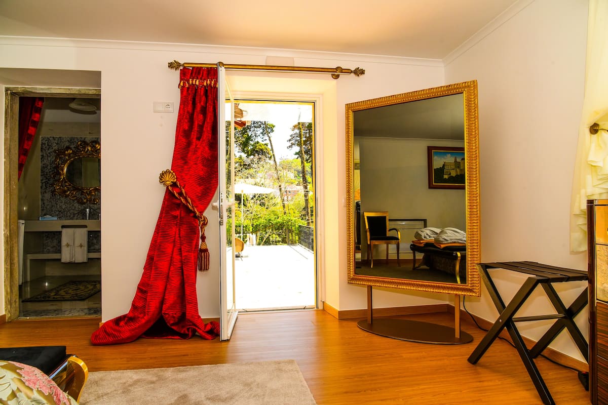 A room with a large mirror, a red curtain, and a view of the outdoors.