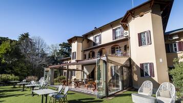 A large, two-story building with a glass-enclosed patio area, outdoor seating, and a well-maintained lawn.