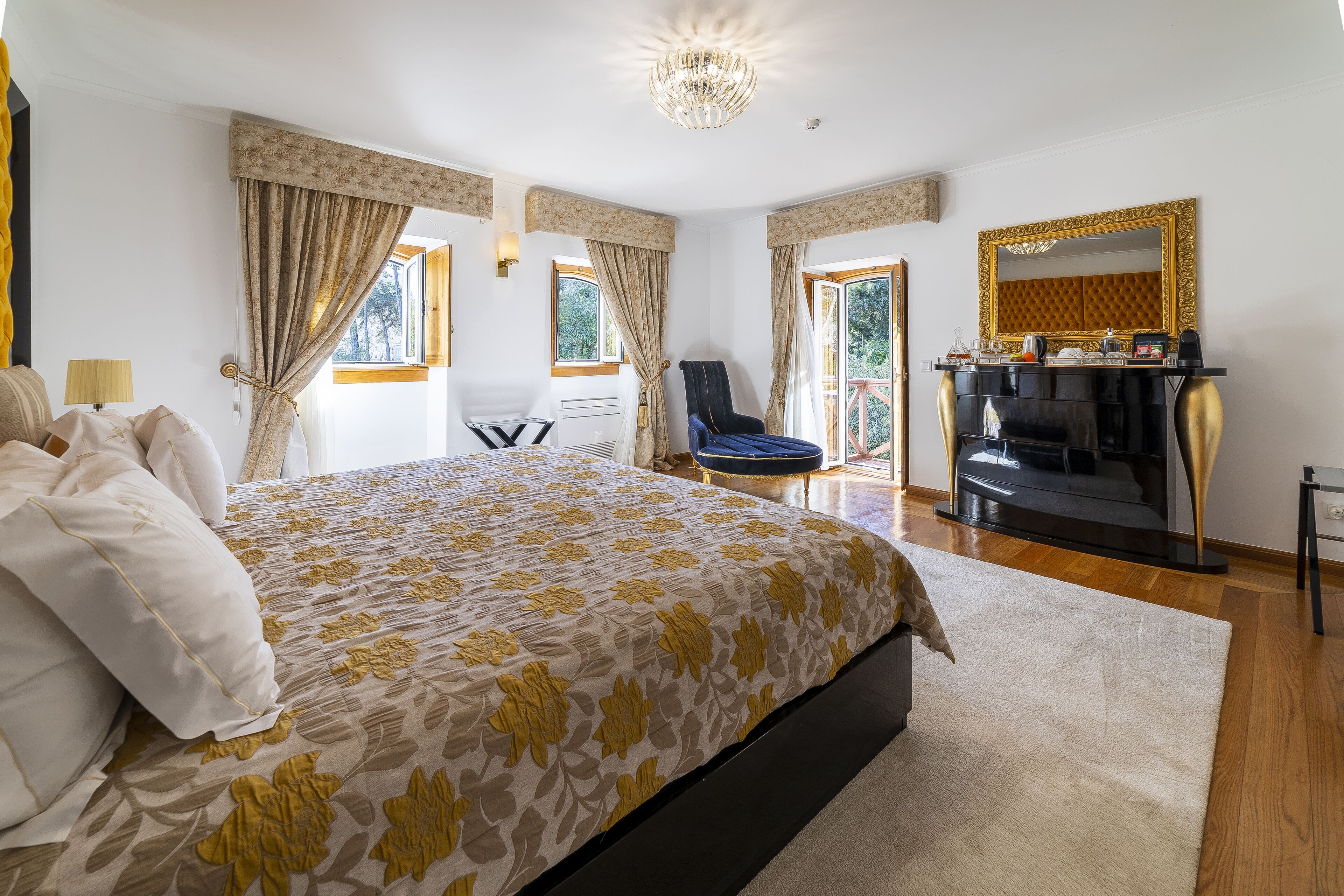 A hotel bedroom with a large bed, a desk, a chair, a TV, and a balcony with a view.