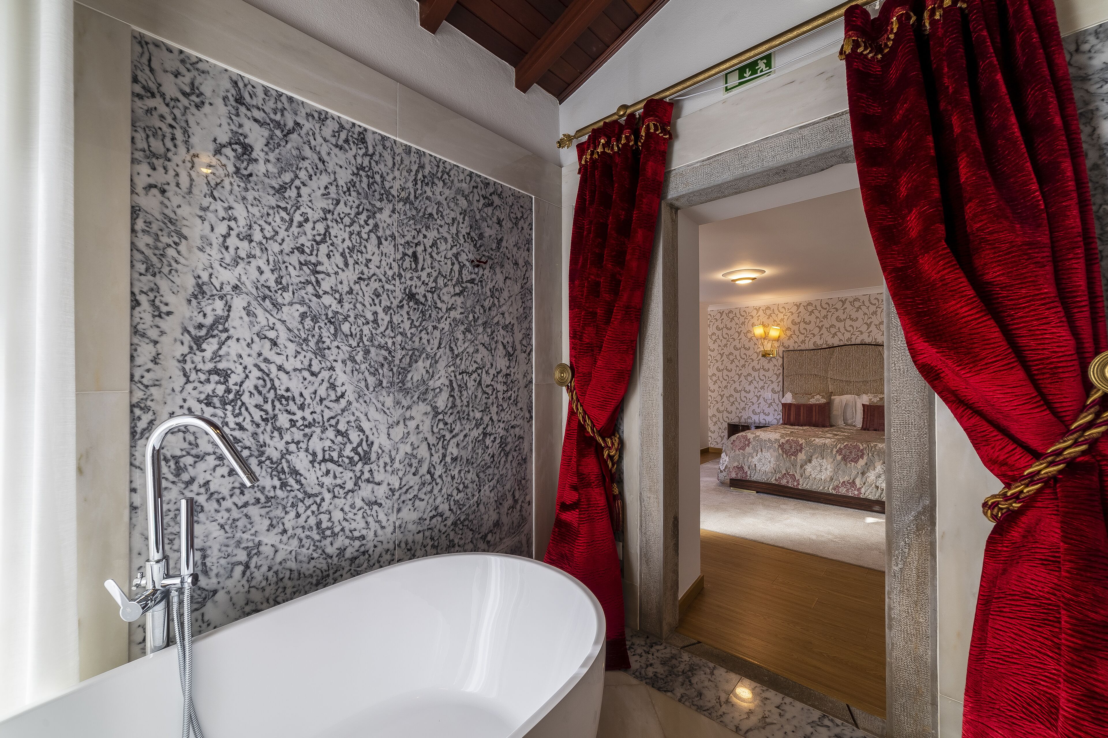 Une salle de bain moderne avec une baignoire sur pieds, un mur en marbre et des rideaux rouges.