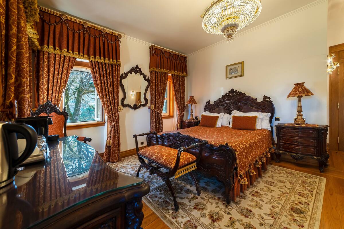 A traditional bedroom with a large bed, ornate curtains, a chandelier, and a wooden nightstand.