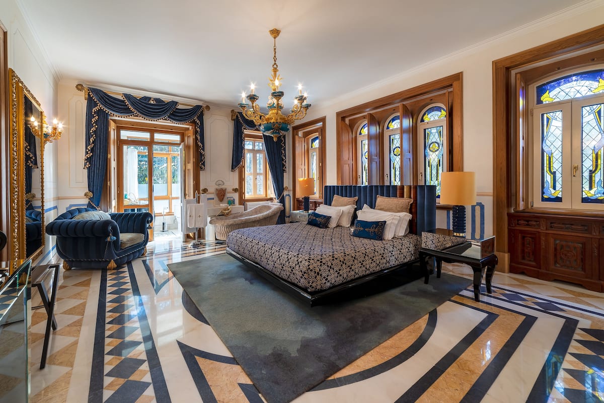 A large bedroom with a king-sized bed, a chandelier, and stained glass windows.