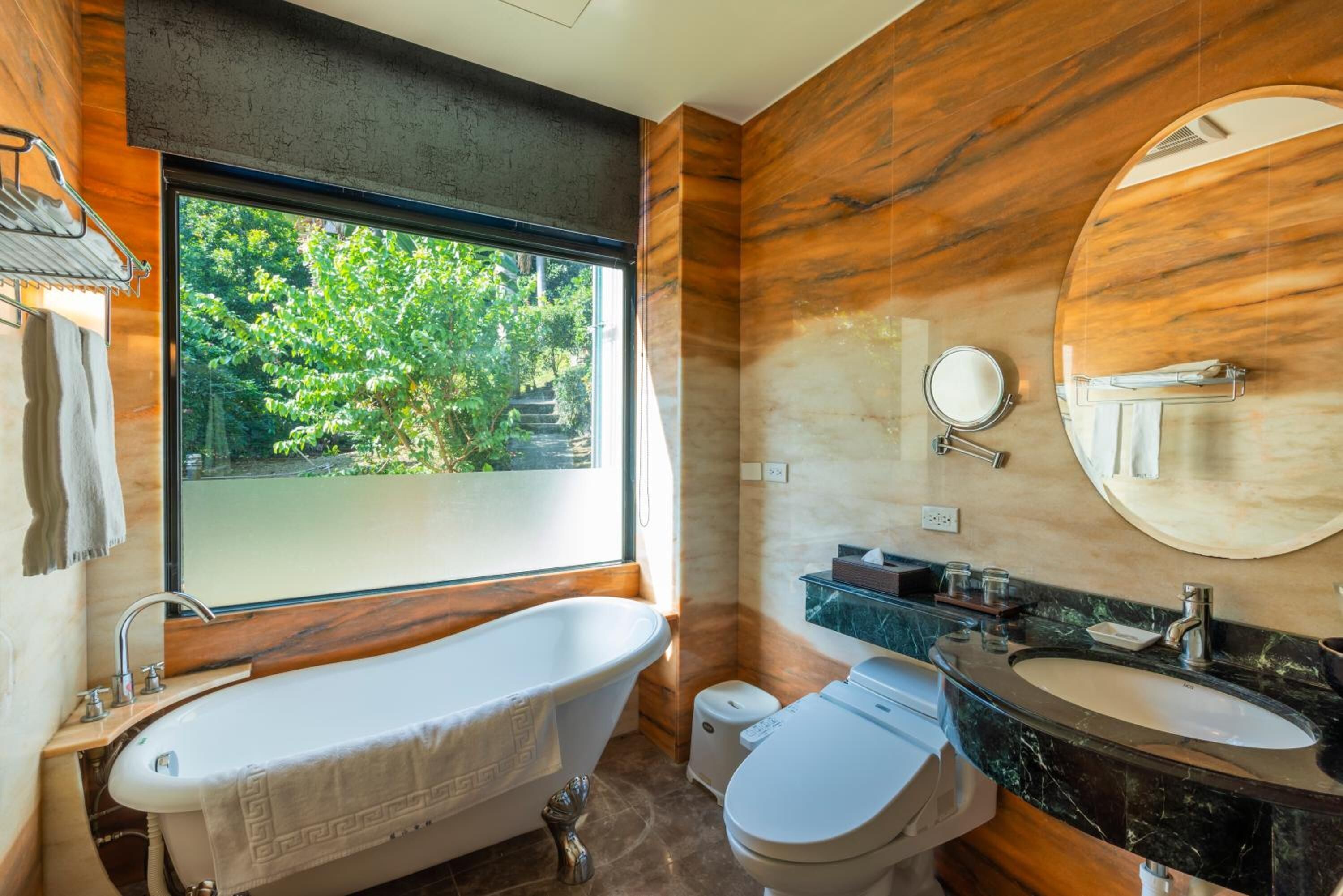 Un baño moderno con una bañera independiente, un inodoro, un lavamanos y un ventanal con vistas a la vegetación.