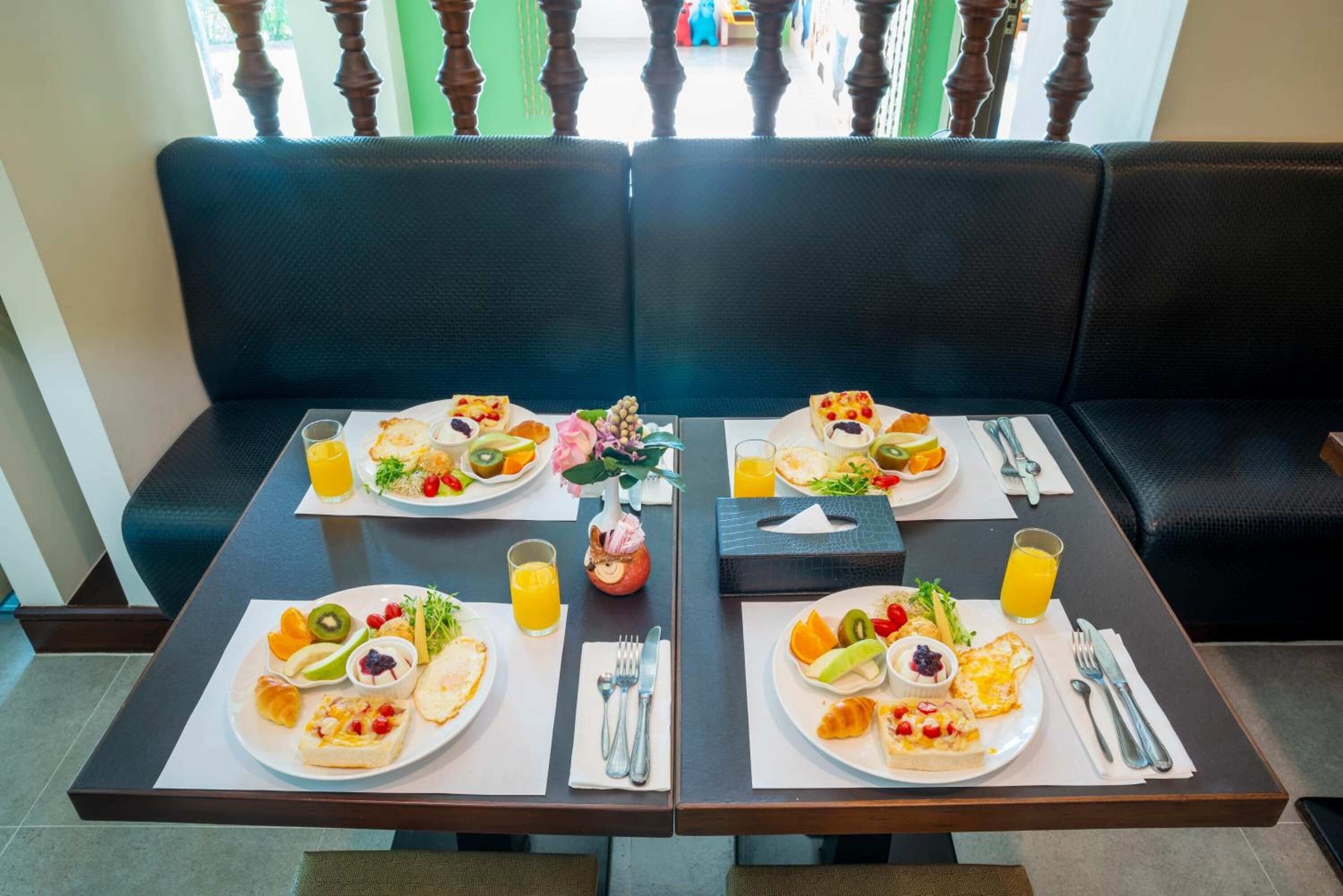 Una mesa de comedor con dos platos de desayuno, cada uno con una variedad de frutas, verduras y pasteles, junto a un vaso de jugo de naranja.