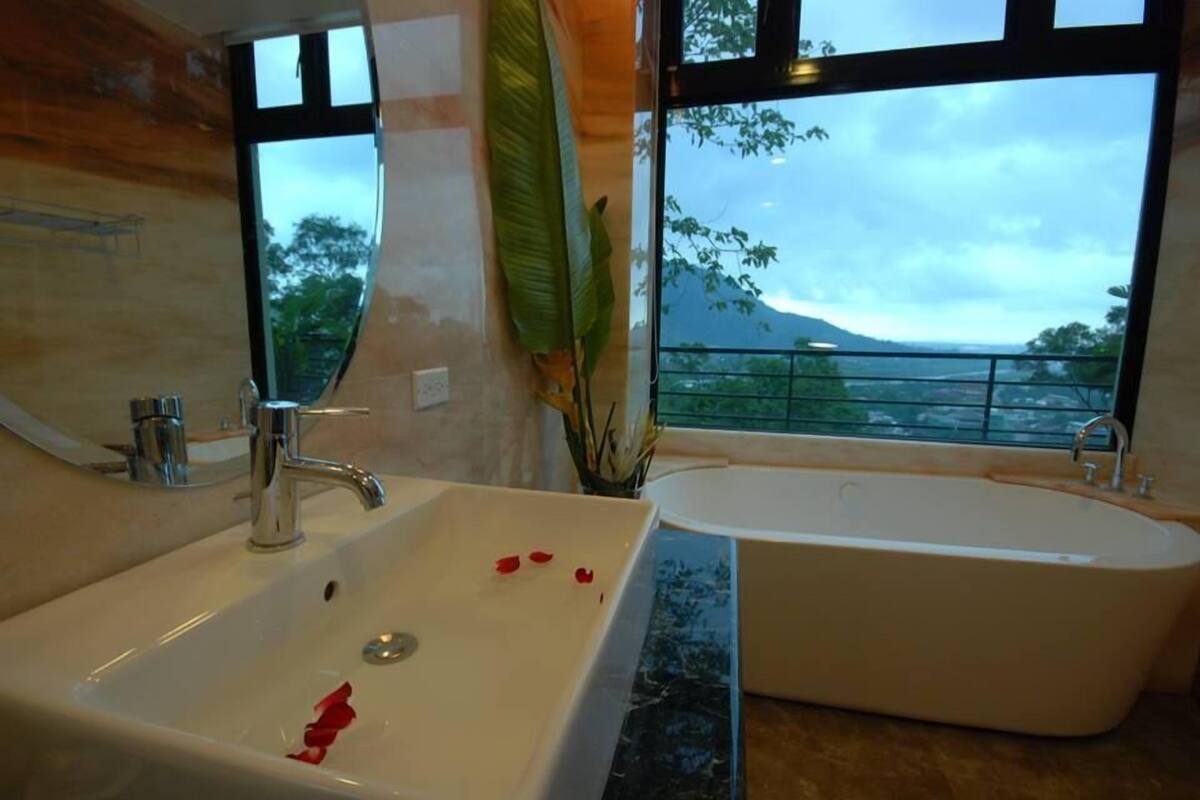 A bathroom with a sink and a bathtub, large windows with a view of a mountain and trees.