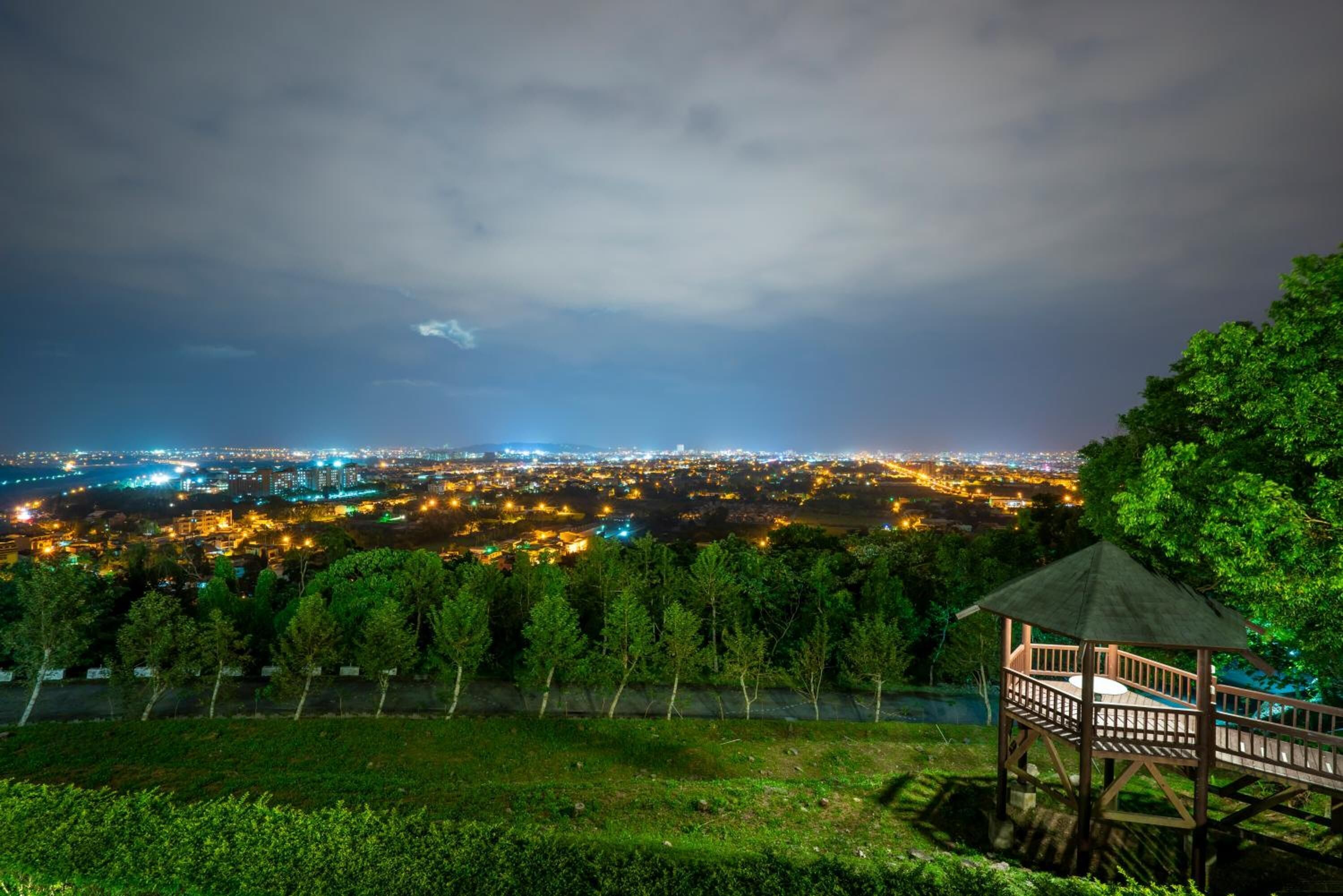 A gazebo with a wooden deck overlooking a cityscape at night.