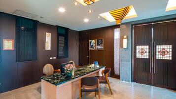 A reception area with a marble counter, two chairs, a vase of flowers, and a dark wooden door with glass panels.