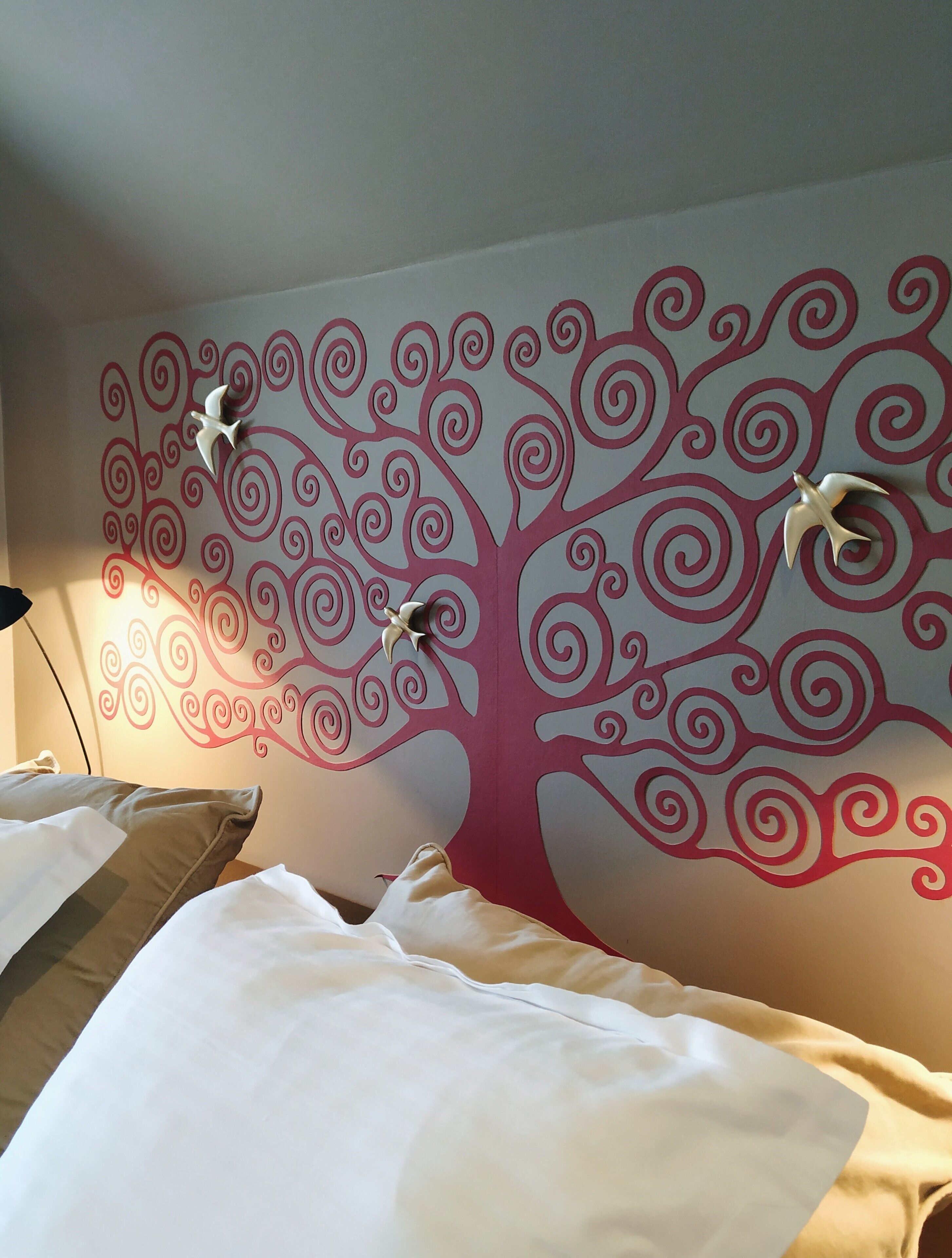 A bedroom with a decorative wall mural of a stylized tree and two white bird sculptures.