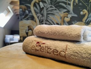 Two rolled towels with the word "Spa" embroidered on them, placed on a bed with a floral wallpaper background. - Hotel Lepelbed Melle (Melle)