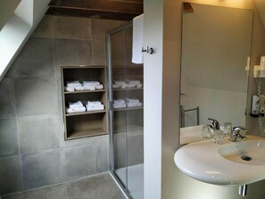 A modern bathroom with a glass shower enclosure, a white sink, and neatly folded towels on shelves. - Hotel Lepelbed Melle (Melle)